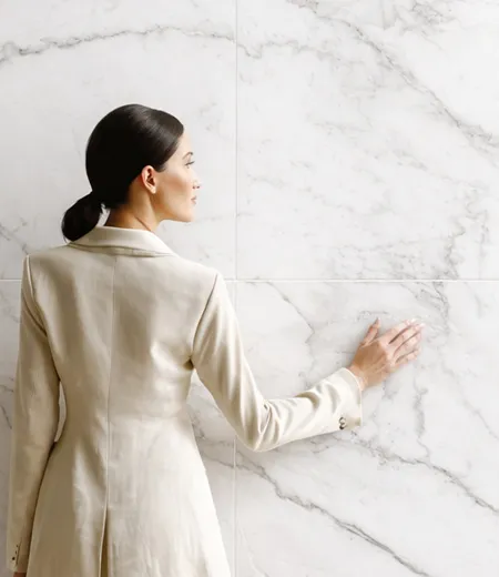 A woman resting her hand on a white marble-look Letoza wall